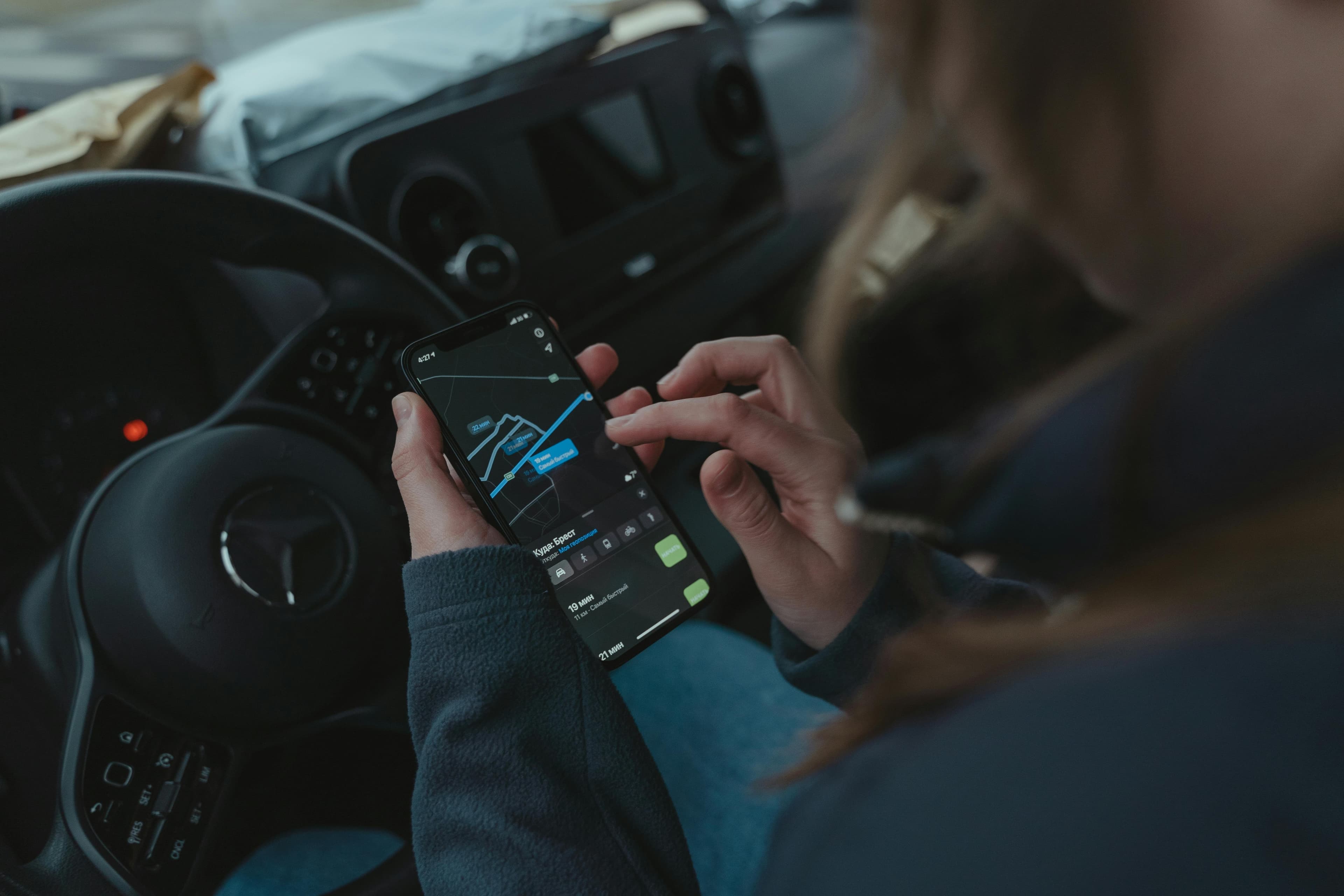 Driver in a car checking a map on their phone, dashboard and steering wheel visible